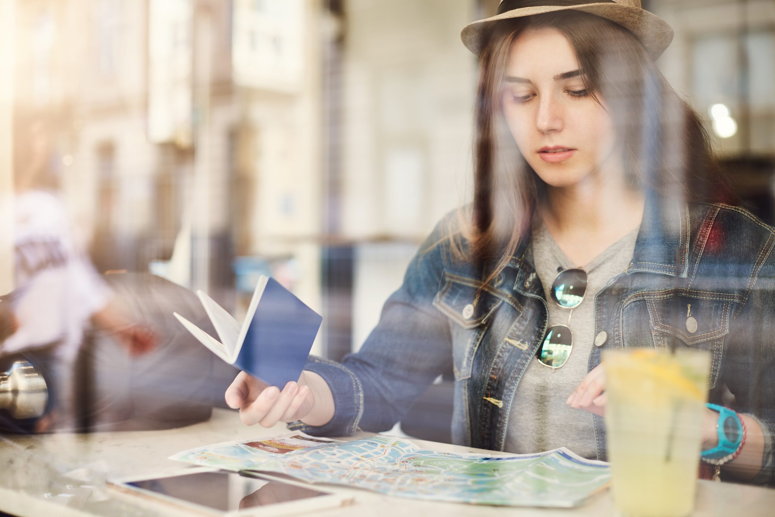 tourist-sitting-cafe-reading-map-holding-passport-drinking-lemonade-busy-city-shot-through-glass-min about-health